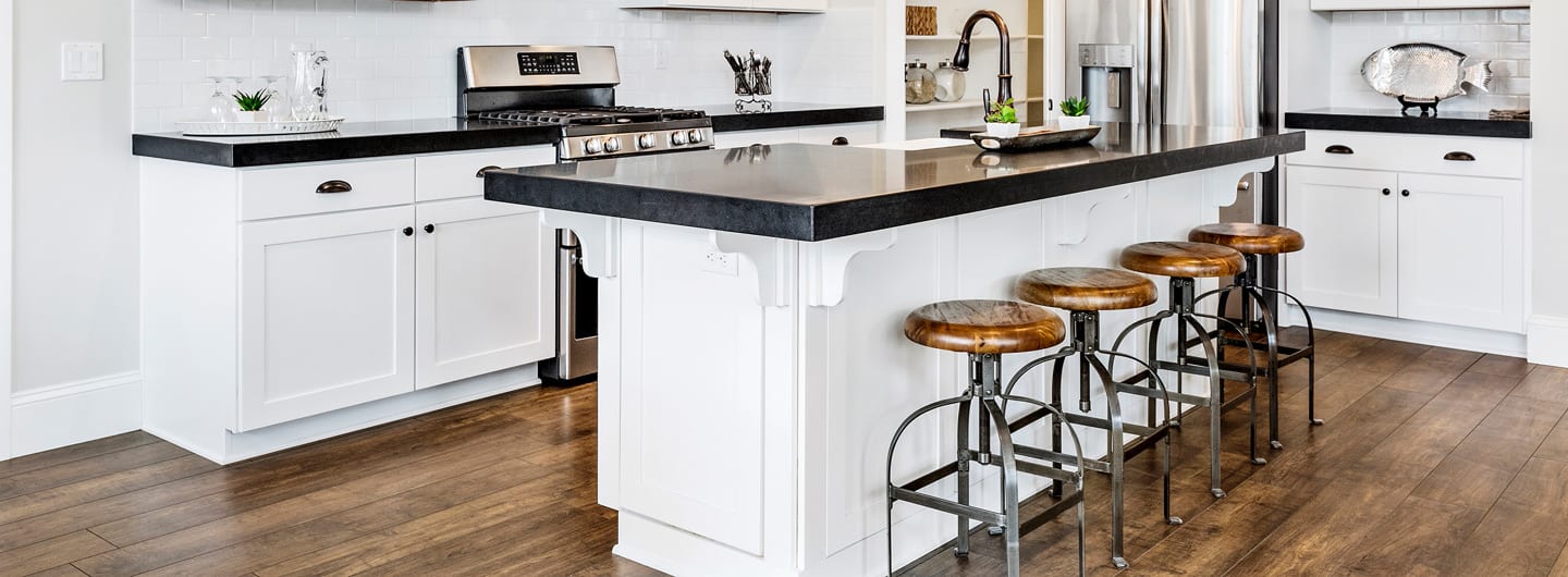 Modern kitchen with white cabinets, a black stone countertop, and four industrial bar stools with brown wood seats